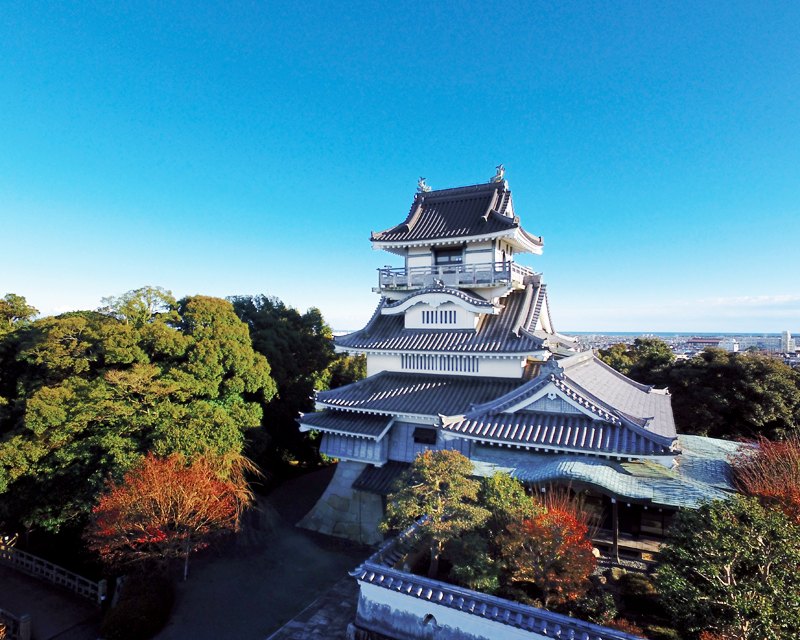 紅葉した木々に囲まれた小山城と、遠くに広がる町並みと海
