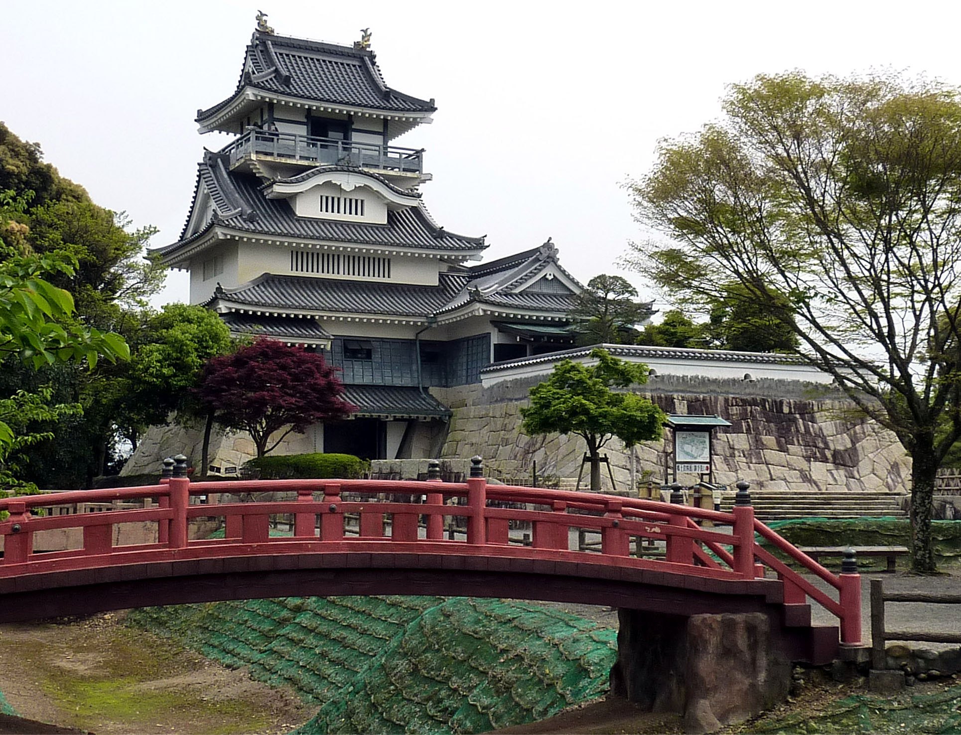 朱色の太鼓橋の奥に建つ小山城と石垣