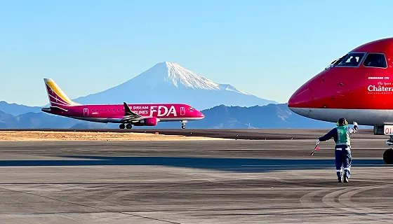 富士山を背に滑走路を進むピンクのFDA機と、手前で誘導する係員