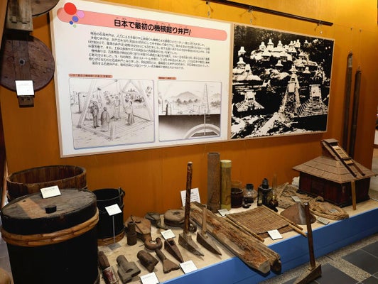 機械掘り井戸の解説パネルと、桶やのみなど石油採掘に使われた道具